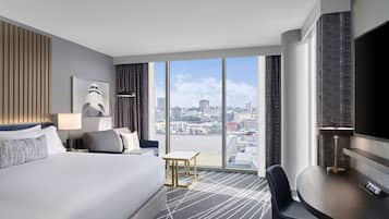 A modern hotel room with a large bed, a desk, and a view of the cityscape.
