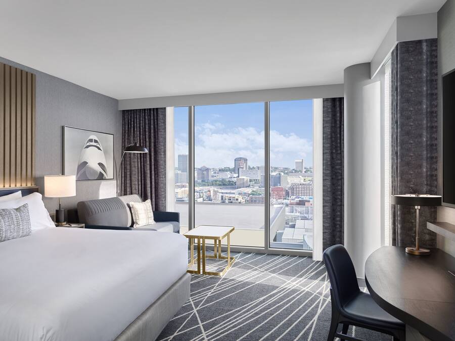 A modern hotel room with a large bed, a desk, and a view of the cityscape.