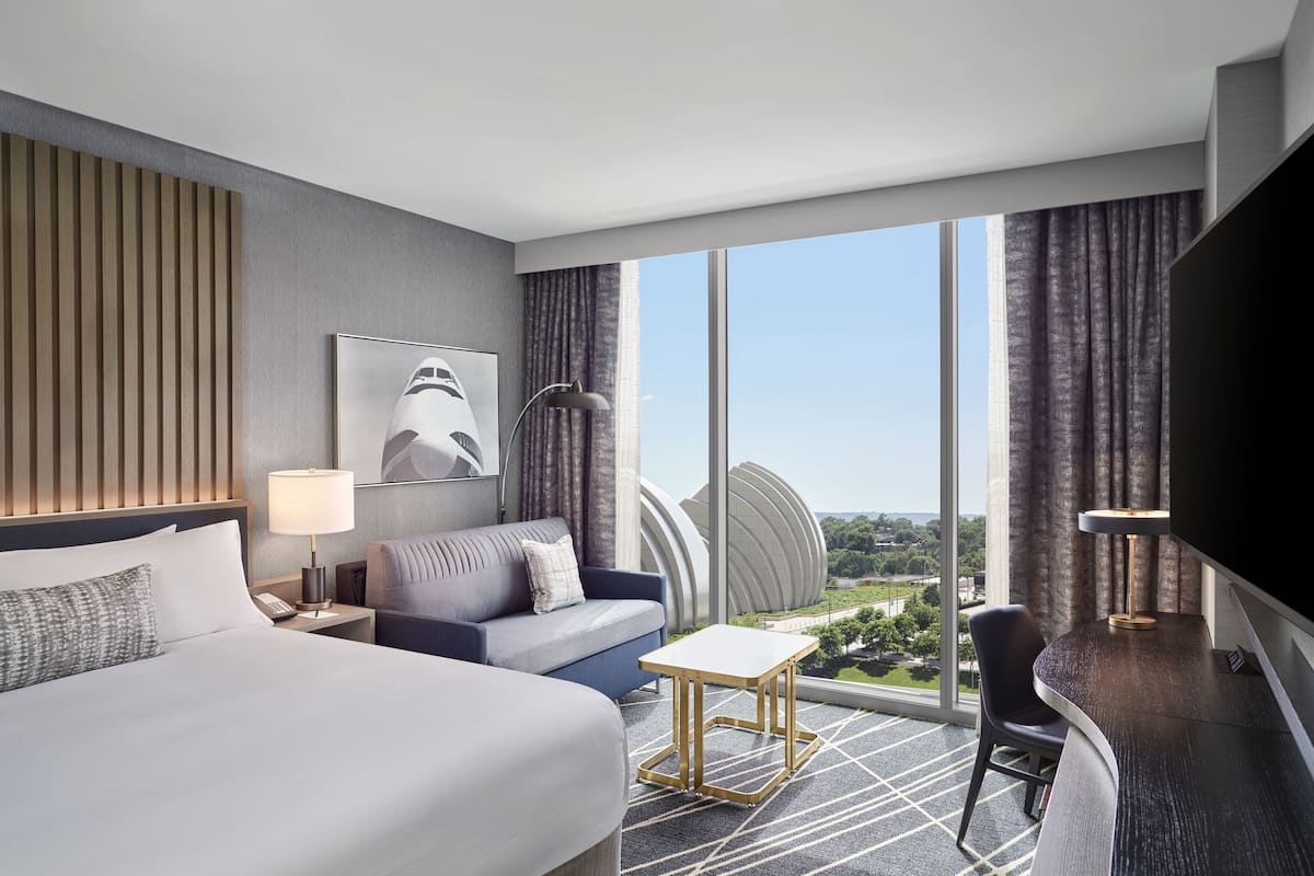 Una habitación de hotel moderna con una cama grande, un sofá, una mesita y un televisor.