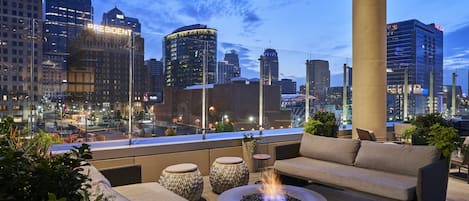 Un salon sur le toit avec des espaces de détente en plein air, un foyer et une vue panoramique sur la ville.
