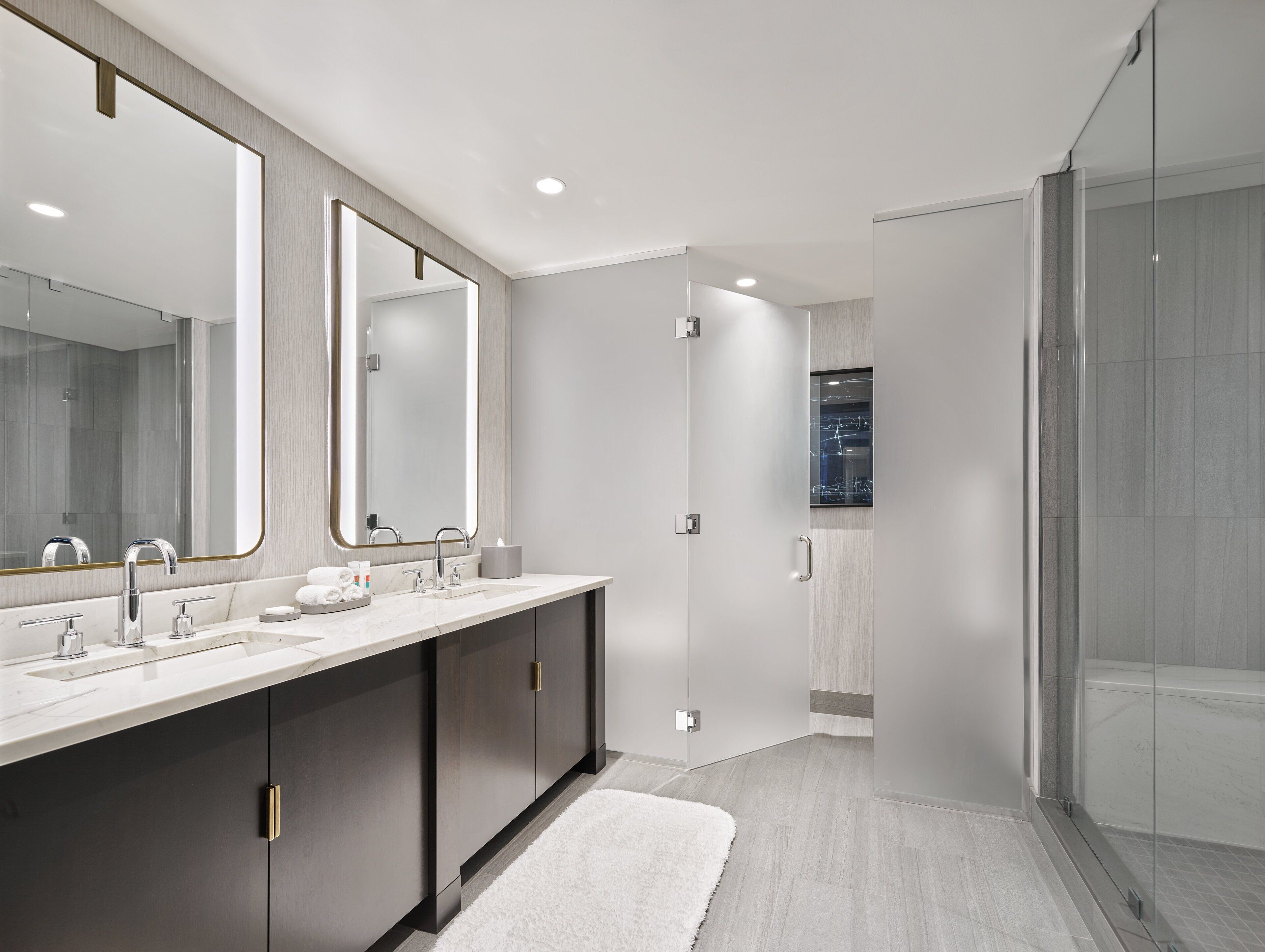 A modern bathroom with a double sink vanity, a large mirror, and a glass shower enclosure.