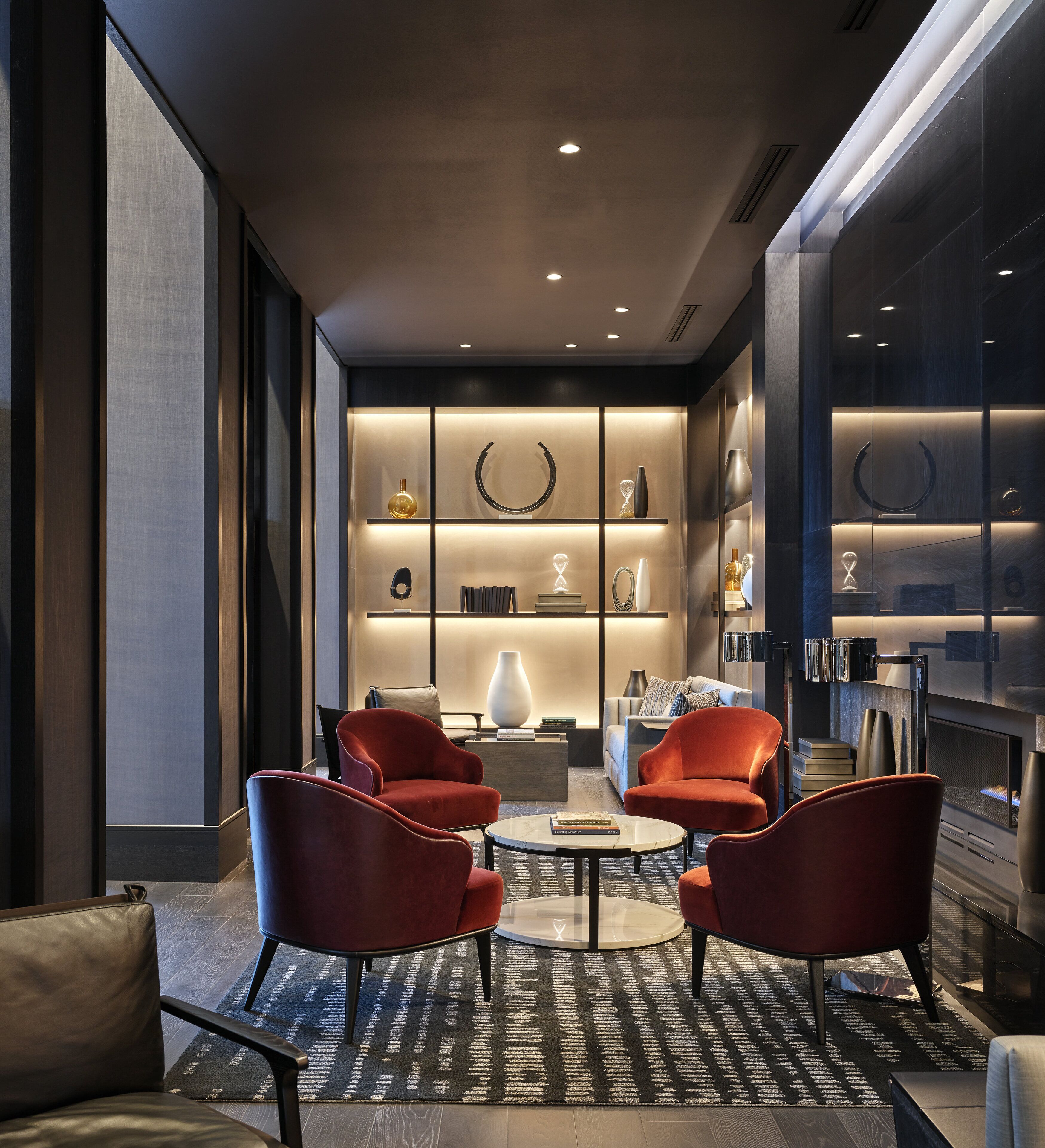 Un salón moderno con chimenea, sillones rojos y una estantería.