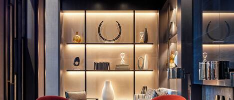 Un interior moderno con una zona de estar que incluye sillas tapizadas en rojo, una mesa de centro de mármol y una estantería con objetos decorativos.