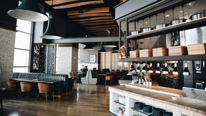 A modern restaurant interior with a wooden bench seating area, a bar counter, and a kitchen visible in the background. - Loews Kansas City Hotel (Kansas City)