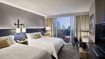 A hotel room with two beds, a desk, a chair, a TV, and a city view.