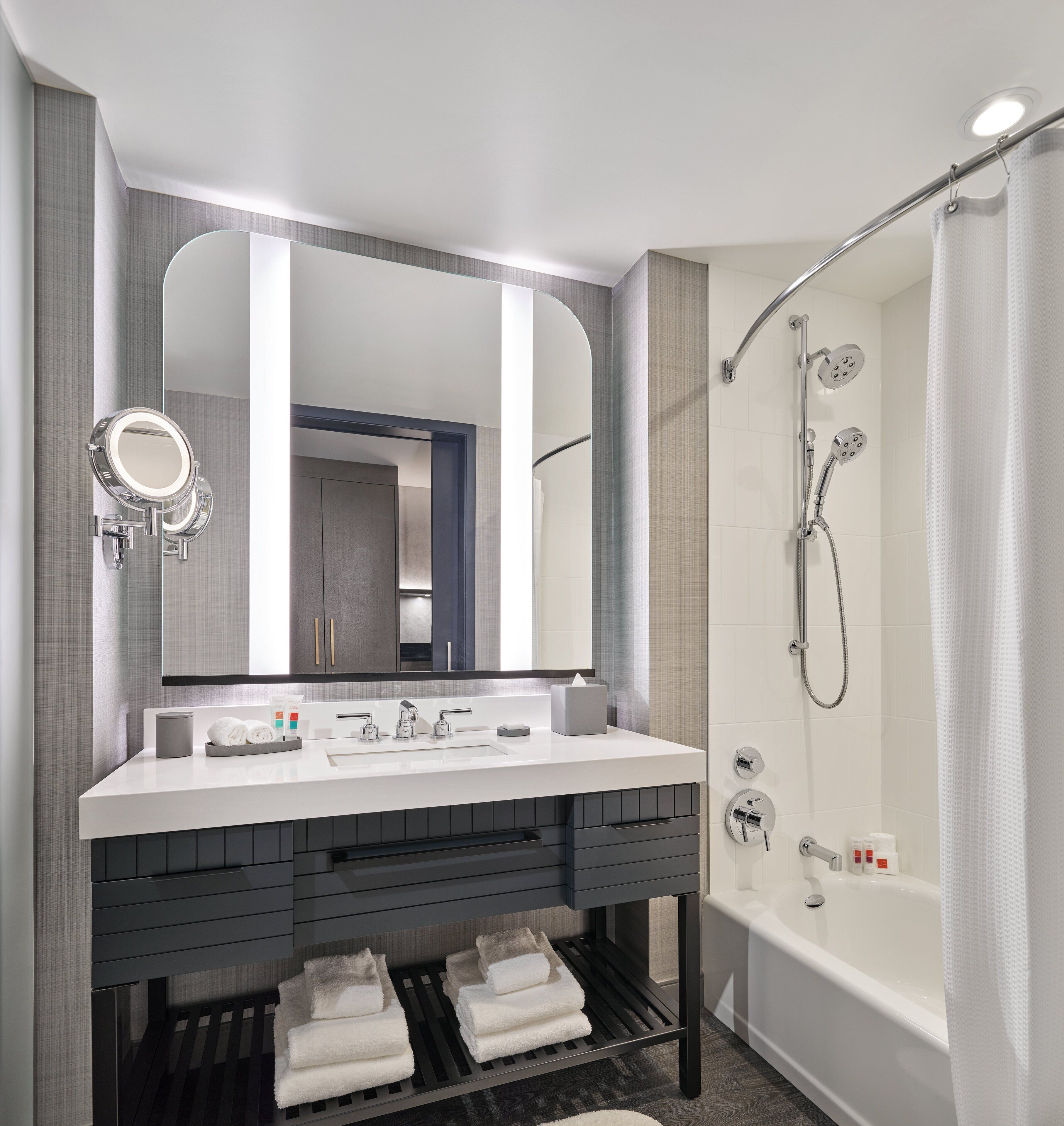 A modern bathroom with a large mirror, a white sink, a shower with a handheld showerhead, and a bathtub.