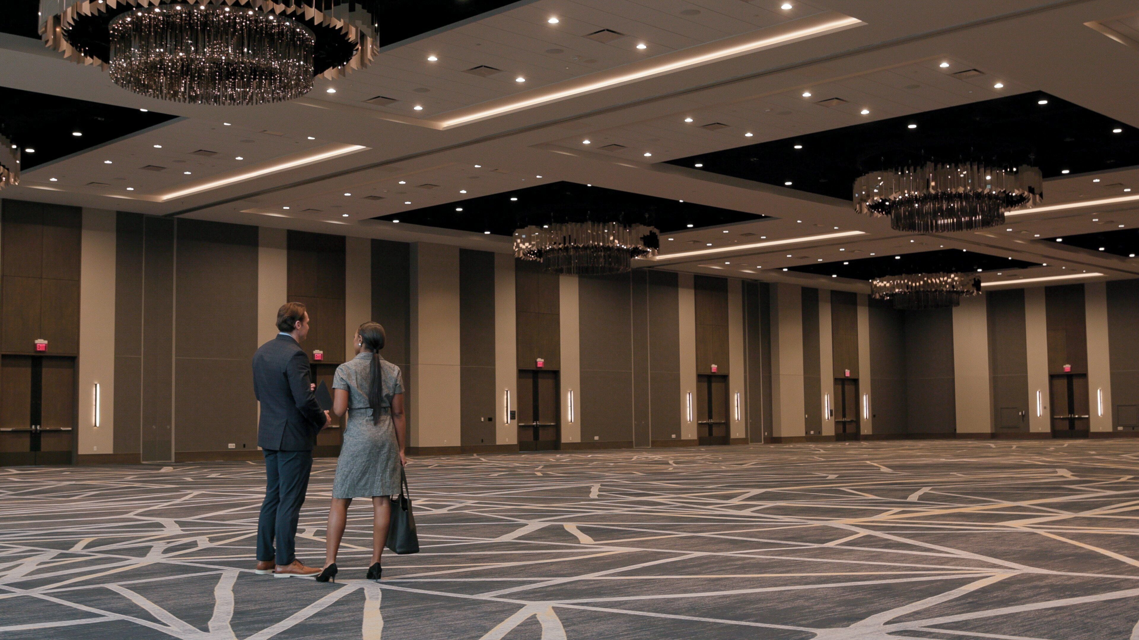 Un amplio vestíbulo de hotel con alfombra de diseño geométrico, varios candelabros y un techo de estilo moderno.