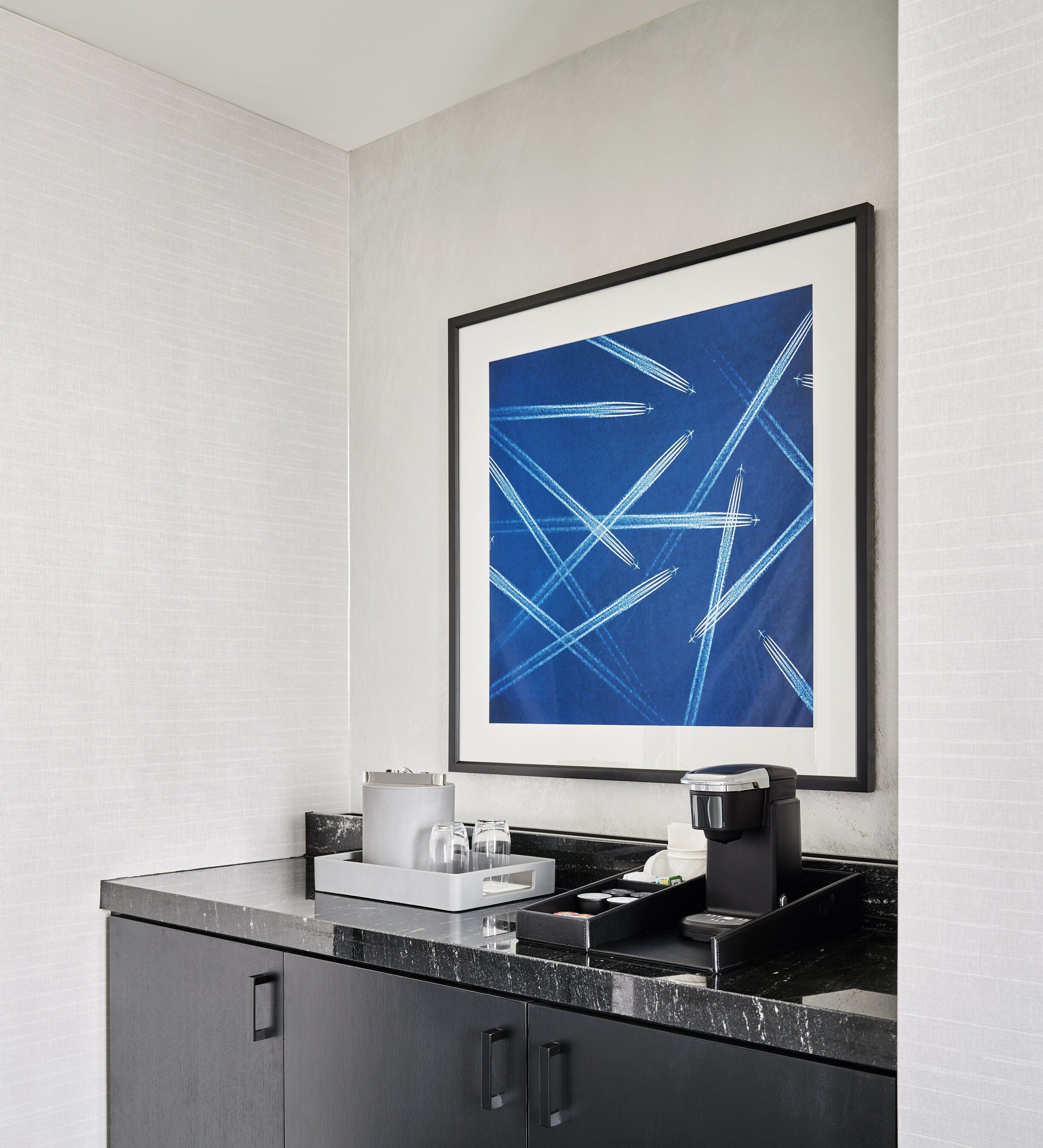 A modern kitchen with a coffee machine, a framed abstract painting, and a marble countertop.