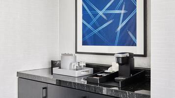 A modern kitchen with a coffee machine, a framed abstract painting, and a marble countertop.