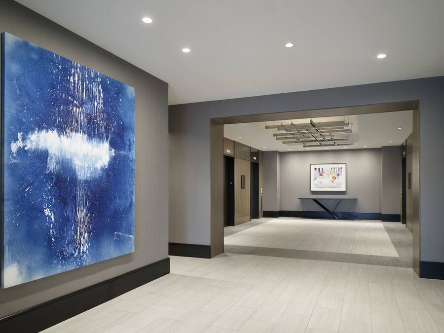 A modern hotel corridor with a large abstract painting, a staircase, and a reception area.