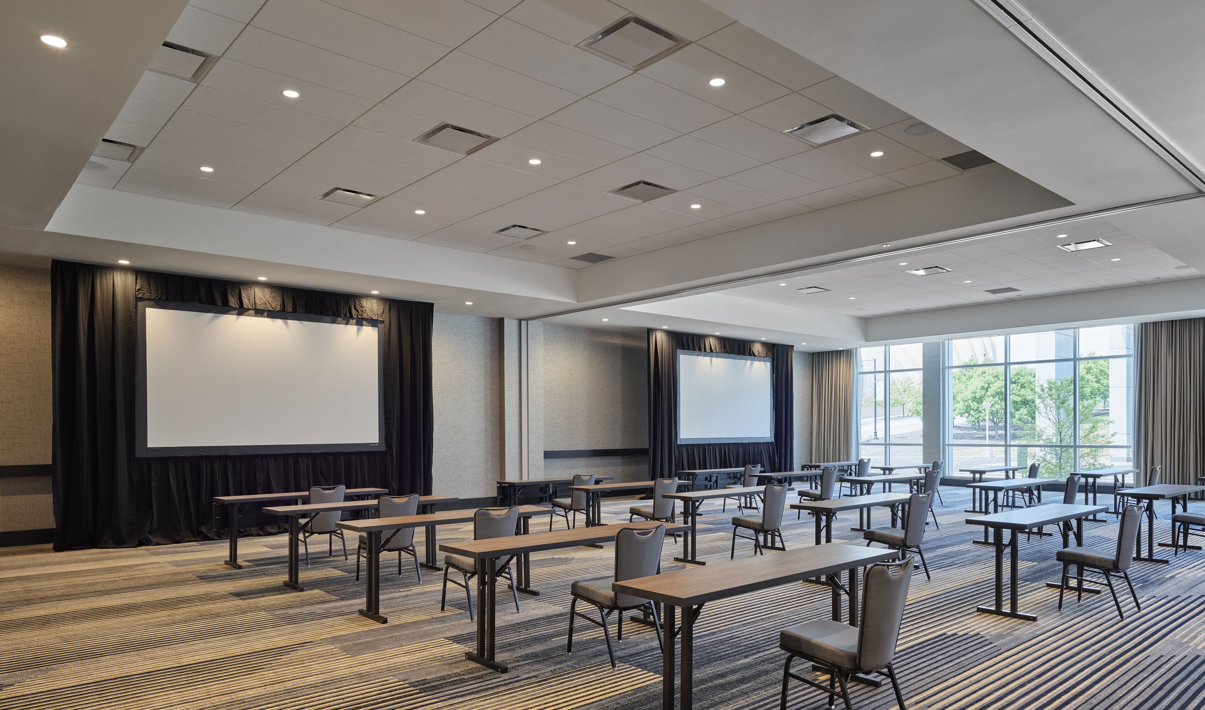 A conference room with multiple tables and chairs, large projection screens, and a carpeted floor.
