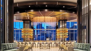 A modern bar area with a central chandelier, seating, and large windows offering city views. - Loews Kansas City Hotel (Kansas City)