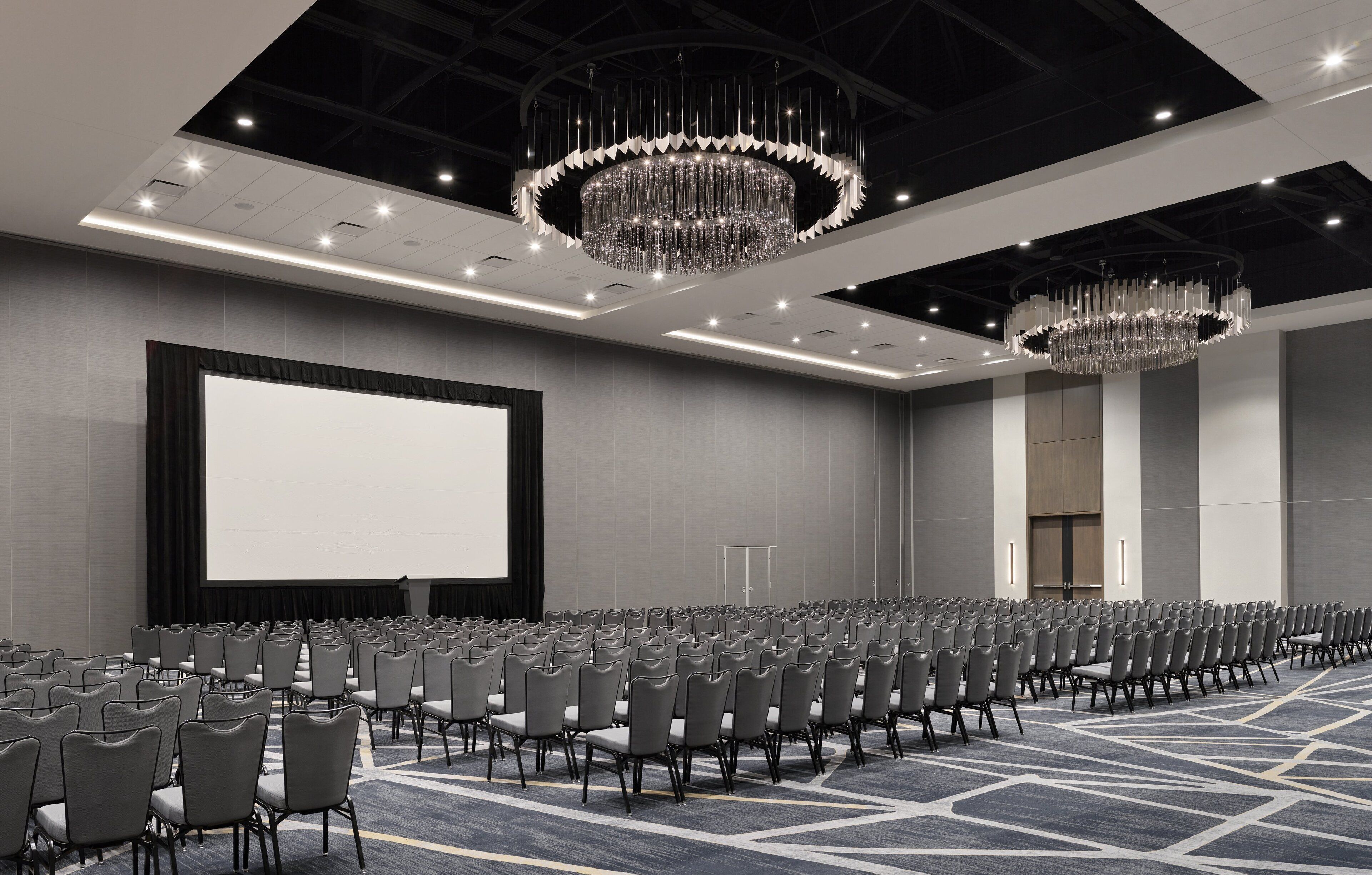 A conference room with rows of chairs, a large screen, and chandeliers.
