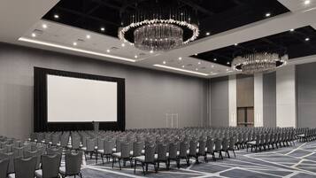 A conference room with rows of chairs, a large screen, and chandeliers.