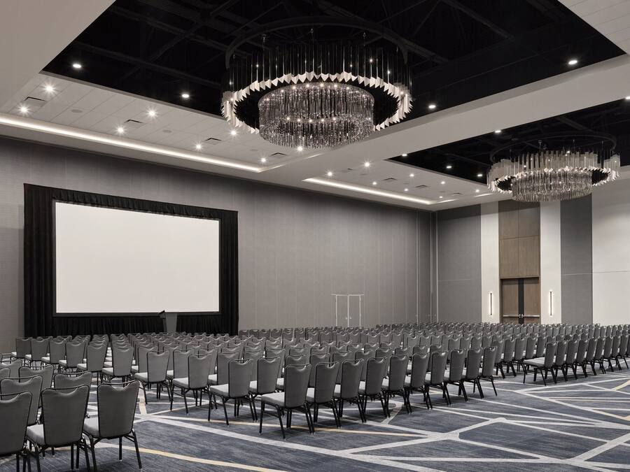 A conference room with rows of chairs, a large screen, and chandeliers.