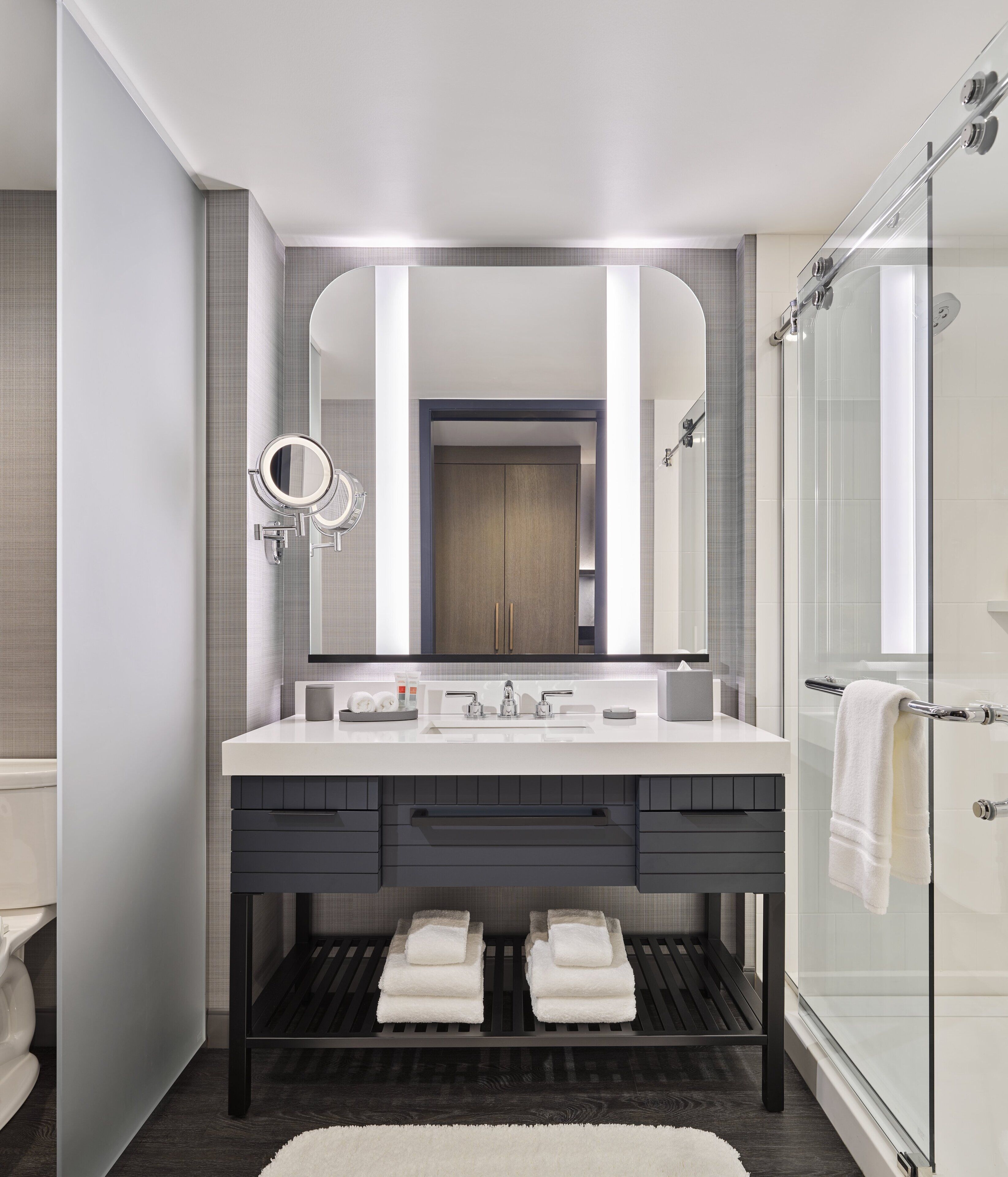 A modern bathroom with a large mirror, dual sinks, and a glass shower enclosure.