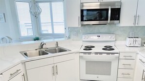 Una cocina moderna con armarios blancos, un lavamanos de acero inoxidable, un microondas, una estufa y un tostador.