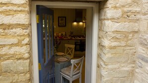 A stone building with a blue door leading to a dining area with a table and chairs. - Converted Luxury Barn - The Potting Shed - Grade II listed (Cirencester)