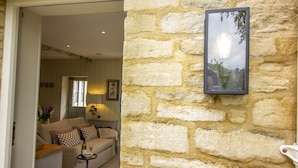 A cozy living room with a stone wall, a framed picture, and a sofa with cushions. - Converted Luxury Barn - The Potting Shed - Grade II listed (Cirencester)