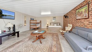 Un salon bien éclairé, avec un canapé, une table basse, un téléviseur, un lit superposé et un mur en briques orné d’un tableau.