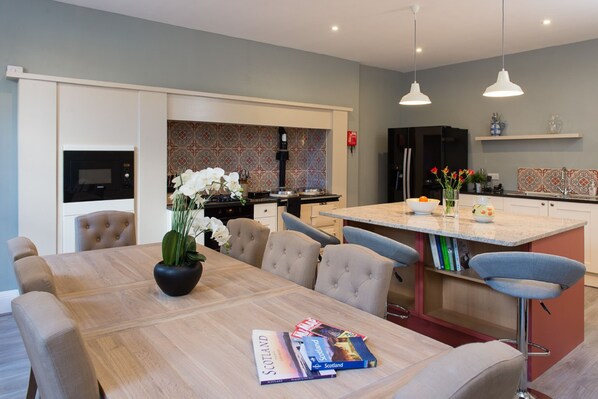 A modern kitchen with a dining area, featuring a large wooden table, comfortable seating, and a central island with bar stools.
