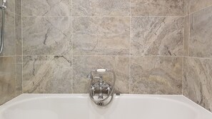 A bathroom with a bathtub, a handheld showerhead, and a wall-mounted faucet.
