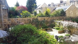 A courtyard with stone walls, lush greenery, and a seating area with outdoor furniture. - Authentic Central 3-Bedroom Apartment (Edinburgh)