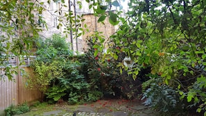 Stroll through the serene garden, surrounded by a variety of plants and flowers, including roses, along a stone pathway.