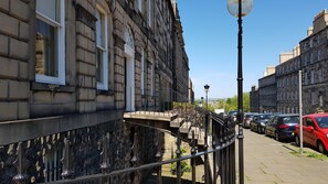 A street with stone buildings, a metal railing, and parked cars.