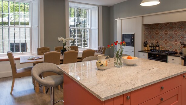 A modern kitchen with a large island, pendant lighting, and a dining area with chairs and a table. - Authentic Central 3-Bedroom Apartment (Edinburgh)
