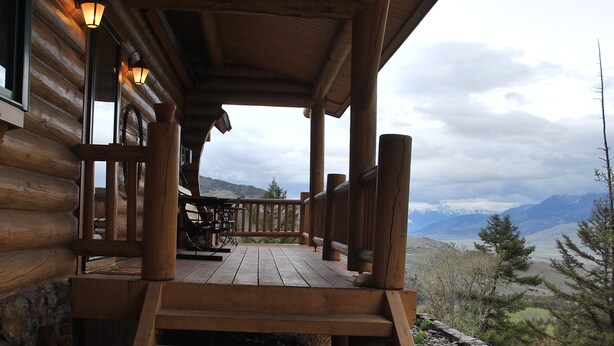 Eine Holzhütte mit Veranda, Treppen führen hinauf, und im Hintergrund sind Berge zu sehen.