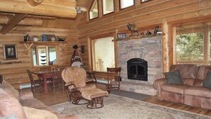 Ein Holzblockhaus-Interieur mit Kamin, Ledermöbeln und einem Essbereich.