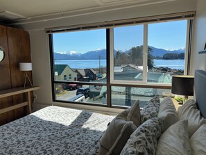 A bedroom with a large window offering a view of a lake and mountains. - Downtown Apt 6 w/ Panoramic Ocean & Mountain Views (Sitka)