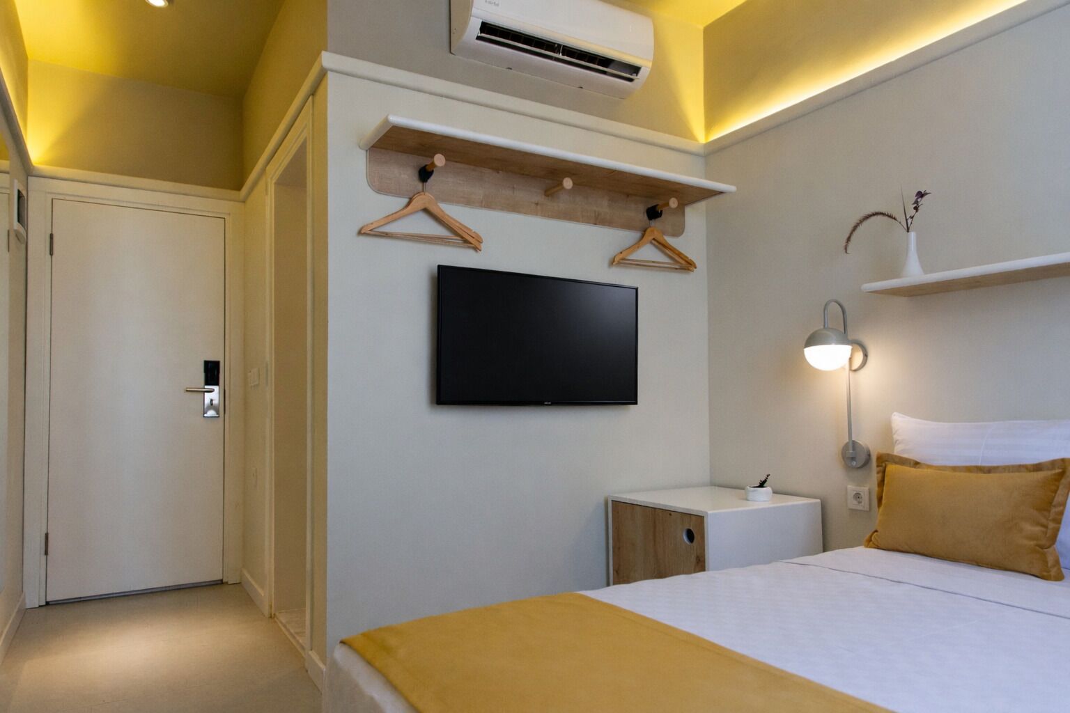 Ein Hotelzimmer mit einem Bett, einem an der Wand befestigten Fernseher, einem Nachttisch, einer Lampe und einem Kleiderschrank.