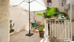 Un pequeño patio con una mesa, sillas, una sombrilla blanca y plantas en macetas.