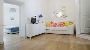 Un salón moderno con un sofá blanco, una mesita de noche con una lámpara y una pared con espejos decorativos.