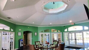 A spacious lobby with green walls, a central seating area with wicker chairs, and a ceiling with recessed lighting and skylights.