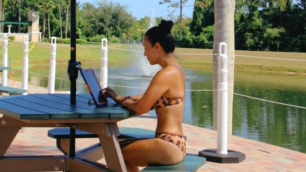 A person sitting at a table under a green umbrella, using a laptop.