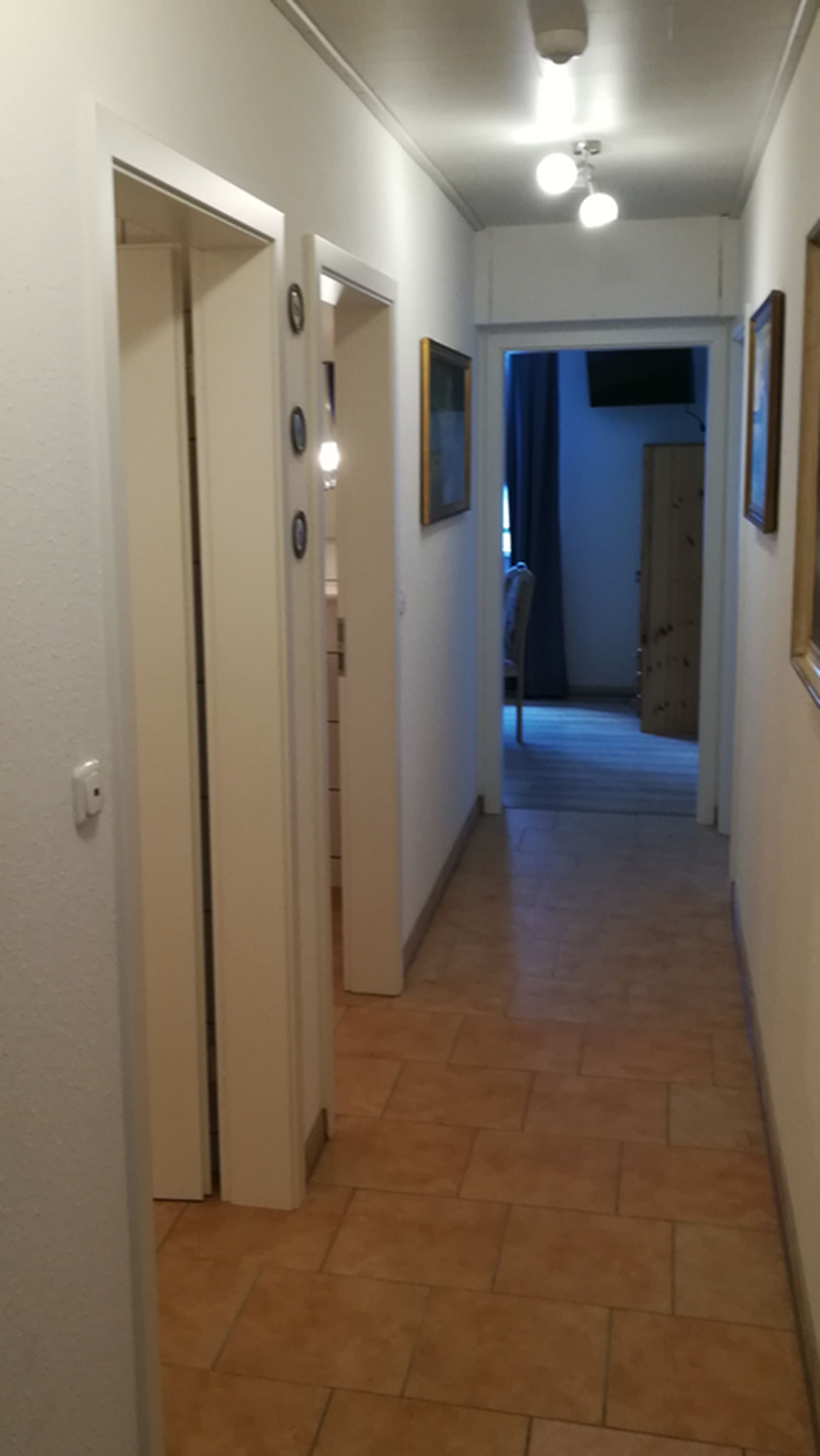 A narrow hallway with tiled flooring, white walls, and several doors leading to different rooms.