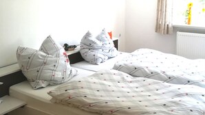 Un lit simple avec une couette à motifs rouges et blancs, une table de chevet et un tableau encadré représentant une jetée, accroché au mur.