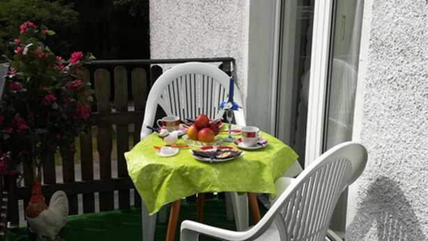 Un petit espace extérieur aménagé pour prendre les repas, avec une table dressée pour deux personnes, des chaises et une nappe verte.