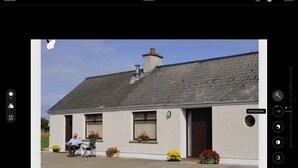 A house with a sloped roof, a chimney, and a door with a window above it. There are potted plants in front of the house. - Porthole Cottage, Bushmills -
 a place to unwind and relax. (Dunseverick)