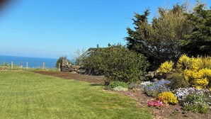 A well-maintained garden with a variety of plants and flowers, a stone wall, and a view of the ocean. - Porthole Cottage, Bushmills -
 a place to unwind and relax. (Dunseverick)