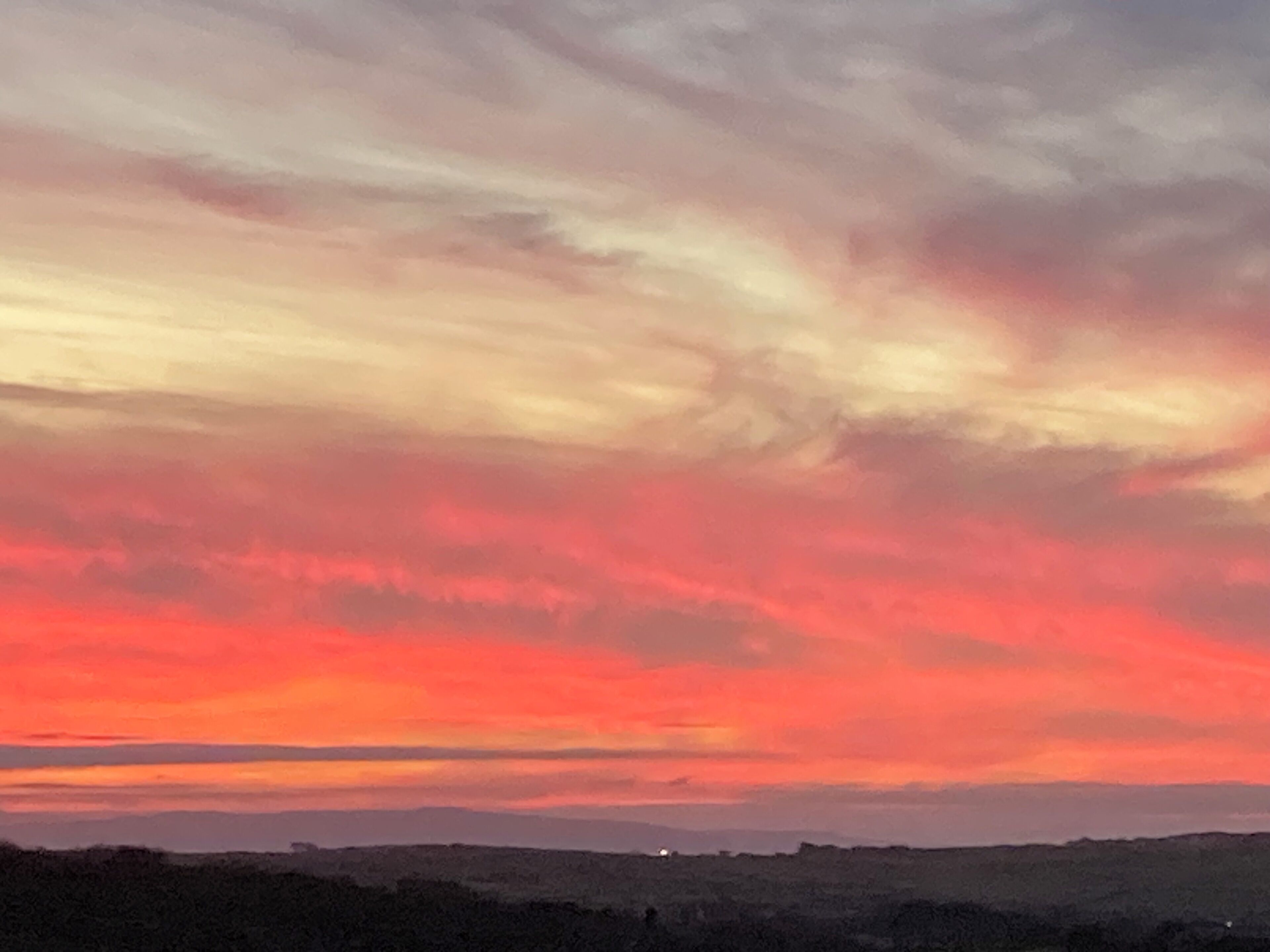 Un coucher de soleil sur un paysage vallonné, avec un ciel dégagé.