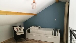 Une petite pièce agréable, dotée d’un plafond en pente, d’un lit simple avec une literie à rayures, d’une chaise avec un coussin et d’un luminaire suspendu.