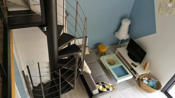 A modern living room with a spiral staircase, a sofa set, a TV, and a small table with a basket of items.