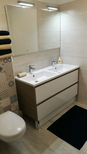 A bathroom with a white sink, two faucets, a mirror above the sink, a toilet, and a patterned shower curtain. - L'alphonsine (Veyre-Monton)