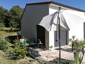 A building with a white exterior and a grey garage door. There is a covered patio area with a table and chairs, and potted plants. - L'alphonsine (Veyre-Monton)