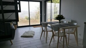 Un espace de salle à manger moderne, avec une table et des chaises, un tapis blanc et une vue dégagée grâce à de grandes portes vitrées.