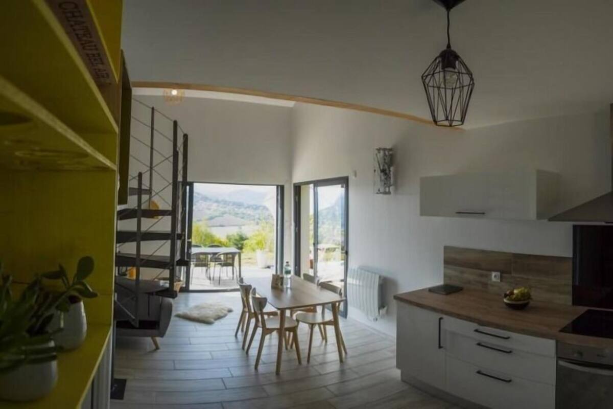 Une cuisine moderne avec un coin repas, de grandes fenêtres et une vue sur l’extérieur.